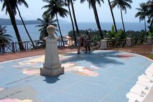 People standing near equator marker with palm trees and the ocean