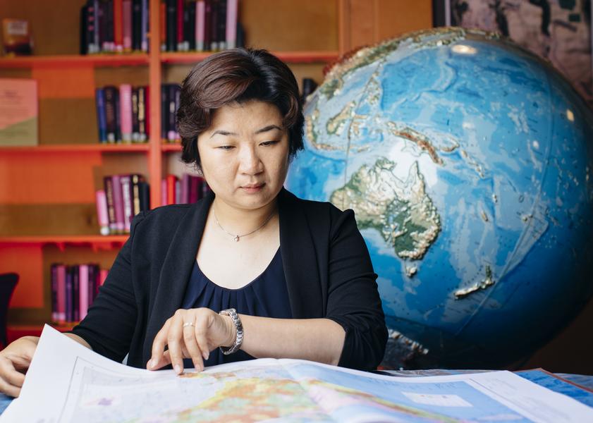 Person paging through a big atlas with a large glove and books in the background.