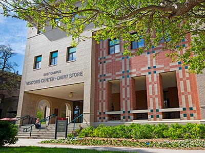 A person sits and eats ice cream from the Dairy Store on the steps of the East Campus Visitors Center on a sunny day.