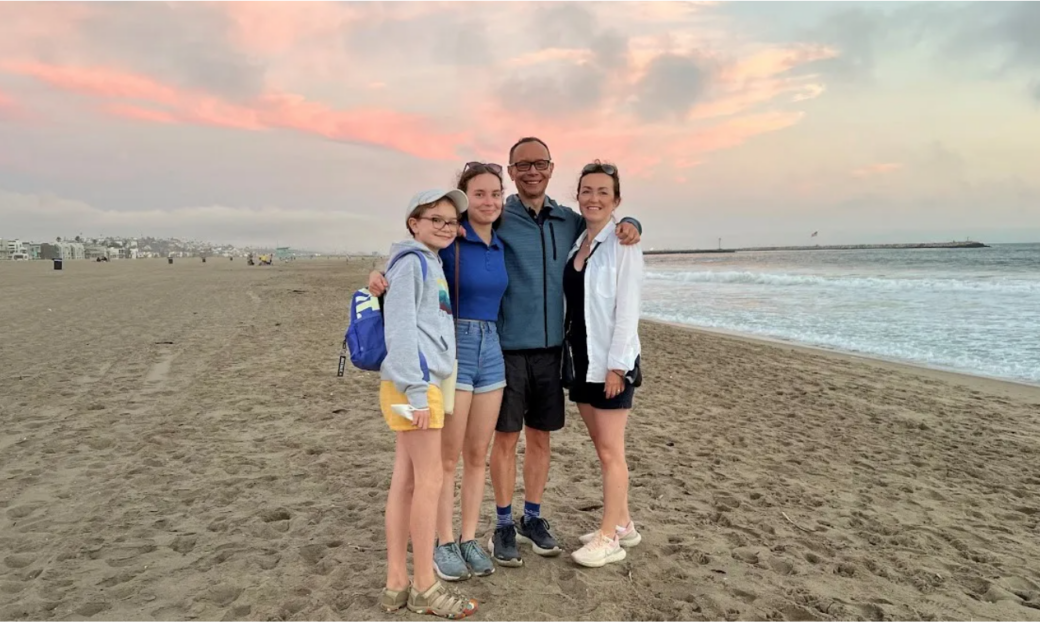 A family of four (a man, a woman and two young girls) standing together at the beach