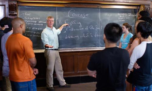 Students in classroom in front of chalk board listening to faculty member.