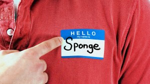 A photo of a man in a red shirt pointing to a name badge which says 'Sponge'.