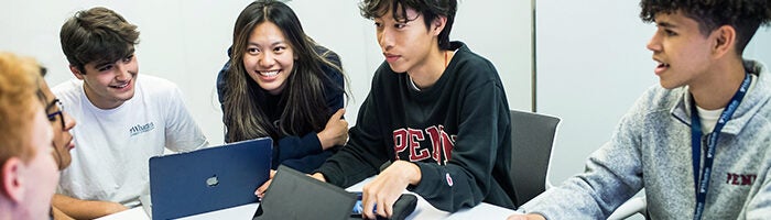 A small group of young people engaged in a collaborative discussion around a table, with laptops open.